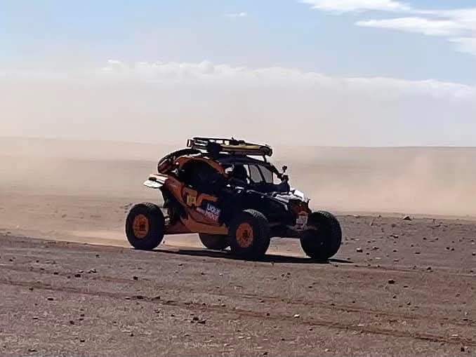 Ein Rallyeauto fährt durch eine staubige Wüstenlandschaft und hinterlässt eine Staubwolke.